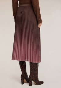 Plisserad midikjol i gradientnyanser av bourgogne och mauve, gjord av fladdrande tyg, i kombination med knähöga, strukturerade bruna ormskinnsboots.