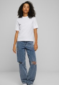 Hvit kortermet t-skjorte kombinert med slitte blå jeans med store hull, brukt stoff, og hvite joggesko. Enkelt og uformelt design.