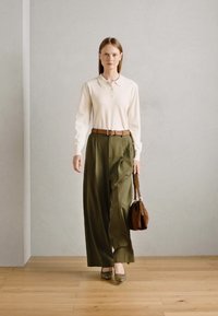 Kremowa koszulka polo z długim rękawem, oliwkowozielone spodnie o wysokim stanie i szerokich nogawkach, brązowy pasek i torebka, wykończone jasnoszarymi balerinami na drewnianej podłodze.
