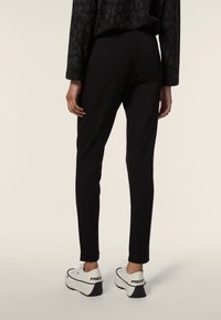 Leggings neri a vestibilità aderente, realizzati in tessuto elasticizzato, abbinati a sneaker bianche con dettagli neri e il marchio "FREDDY".