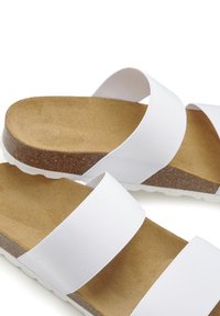 Witte instapsandalen met twee brede stofbanden en een kurken voetbed. Gevoelige bruine oppervlakte en witte rubberen zool zorgen voor comfort.