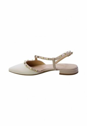 Scarpa piatta a punta in crema con cinturini beige. Presenta borchie a piramide dorate lungo il cinturino e un tacco basso per stabilità.