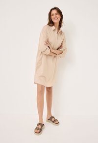 Light beige button-up shirt dress with rolled sleeves, tailored fit, and side slits. Paired with leopard print slide sandals.