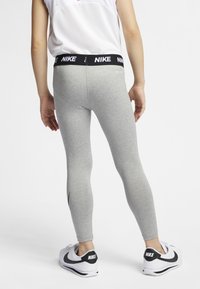 Gray leggings made of stretchy material with a black Nike logo waistband; worn with white sneakers featuring black accents and a smooth texture.