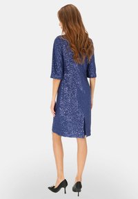 Granatowa sukienka z cekinami, rękawy do łokcia, długość do kolan, z rozcięciem z tyłu. Noszona z czarnymi szpilkami.