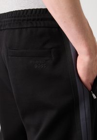 Melnas sporta bikses ar elastīgu jostasvietu, ar aizmugurējo kabatu un izšūtu "Porsche BOSS" logotipu, papildinātas ar sānu līnijām.