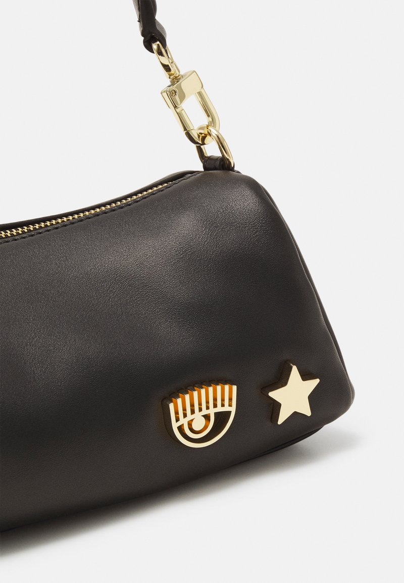 Black leather handbag with a gold zipper, featuring a geometric eye detail and a star-shaped accent. Smooth texture and structured shape.