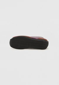 Chanclas moradas con un upper texturizado, que cuentan con una suela de goma marrón y un patrón de banda de rodadura ondulado para el agarre. Diseño minimalista con acentos funcionales.
