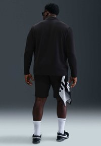 Svart langermet skjorte med krage, et par svarte shorts, hvite sokker og svarte joggesko. Et håndkle med svart og hvitt design er drapert over armen.