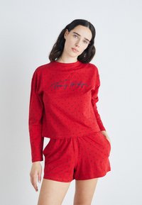 Röd loungeklädsset med långärmad topp och shorts, med marinblåa prickar och en framsida med logotyp i kursiv stil. Mjuk, stretchy tyg.