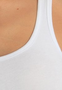 White tank top, cotton material, fitted design, round neckline, soft texture, featuring simple stitching along the edges.