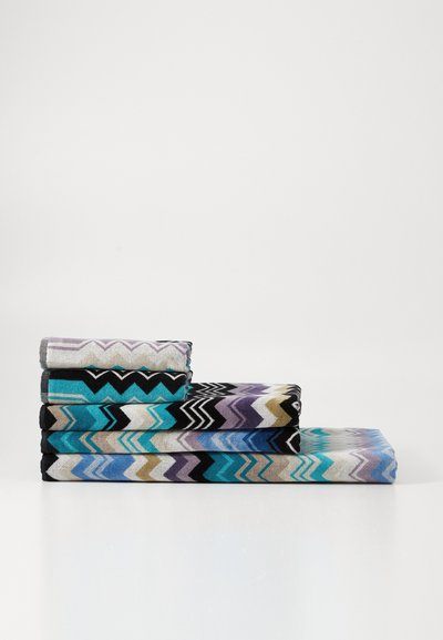 Pila di cinque asciugamani decorati in vari colori, con motivi a zigzag in blu, nero, viola e beige. Texture morbida, forma rettangolare.