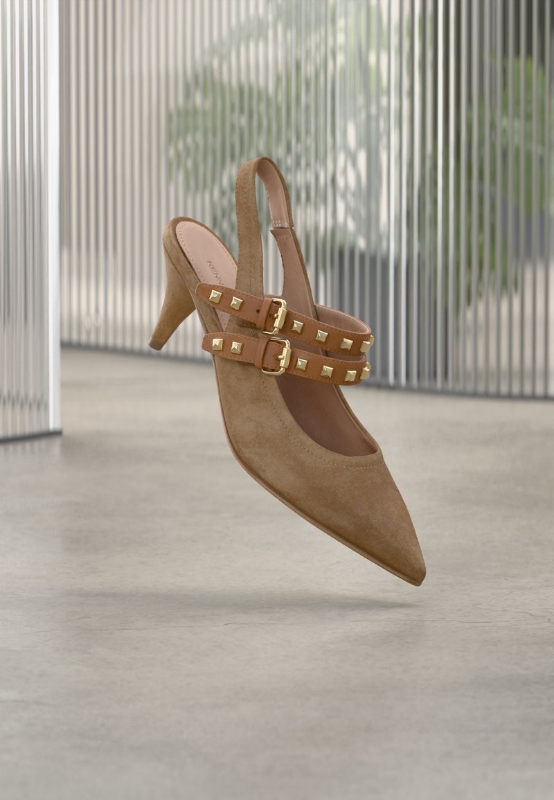 Μπεζ σουέντ πέδιλο με λουράκι στο πίσω μέρος, μυτερή μύτη, με διπλούς ιμάντες με αγκράφες διακοσμημένους με χρυσές πυραμιδωτές τρουκς. Σχεδιασμός με ανυψωμένη σόλα.