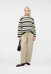 Triibuline must ja kreemjas kampsun, beežid paeltega püksid, must käekott ja burgundi punased mokassiinid. Kampsunil on mugav lõige ja ribakujuline tekstuur.