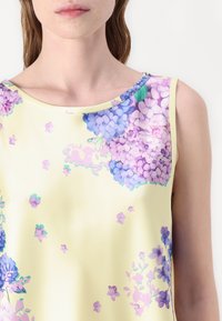 Top sin mangas de tejido suave con un fondo amarillo pálido y patrones florales morados. Cuello redondo destacado y corte relajado.