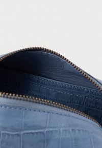 Zila teksturēta ādas soma ar gludu oderi un kontrastējošu šuvumu, augšējā rāvējslēdzēja aizdare un bronzas detaļas.