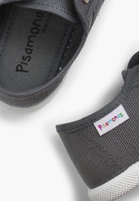 Zapatos de lona grises con una superficie texturizada, suelas de goma blancas y una etiqueta colorida de "Pisamonas" en el costado.
