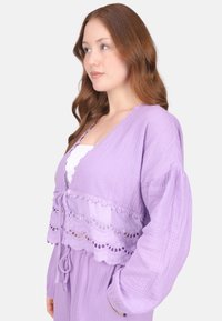 Lavendelfarbenes, strukturiertes Strickjacke mit einem cropped Design, ausgestattet mit einer gewellten Spitzenborte und voluminösen Ärmeln, die vorne gebunden ist.