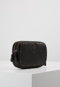 Bustina in pelle nera con doppia cerniera, forma arrotondata, superficie testurizzata e borchie decorative colorate lungo i bordi. Logo visibile sul davanti.