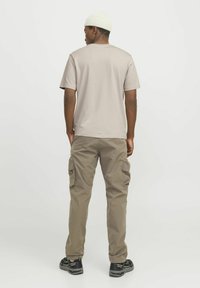 Camiseta beige de manga corta, combinada con pantalones cargo caquis que tienen bolsillos laterales. El atuendo se complementa con un gorro blanco de punto y zapatos negros.