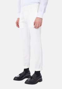 Pantaloni bianchi su misura con una texture liscia, caratterizzati da una vestibilità slim e orli risvoltati, abbinati a mocassini neri lucidi e calzini.