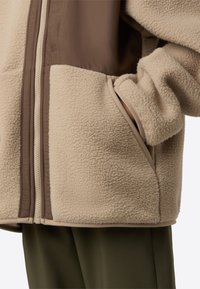 Beežist fliisist jakk pruunide nailondetailidega, eest tõmblukuga ja küljetaskutega. Pehme tekstuur kontrastse äärisega servadel.