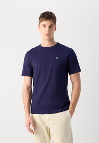 Marineblå bomulds T-shirt med korte ærmer, rund halsudskæring og hvid logo detaljer på brystet. Glat tekstur og tætsiddende pasform.