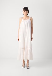 Vestido blanco sin mangas con cuerpo fruncido, ribete de encaje en el dobladillo y detalles de ojal. La modelo lleva zapatos plateados metálicos. Corte simple y holgado.