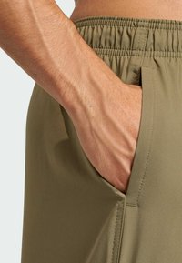 Olivově zelené kraťasy s elastickým pasem a boční kapsou, které se vyznačují hladkým povrchem a čistými švy.