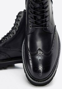 Czarne skórzane buty za kostkę z sznurowanym zapięciem, z detalami w stylu brogue, podniesionym noskiem i teksturowaną podeszwą dla lepszej przyczepności.