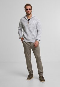 Grijze gebreide pullover met een kwart-rits kraag en een gestructureerd patroon, gecombineerd met beige taps toelopende broek en bruine moccasin-stijl schoenen.
