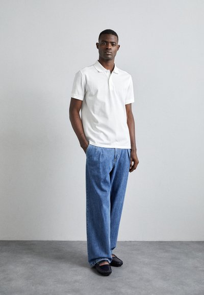 Camisa polo blanca, jeans azules holgados y zapatos negros. Diseño simple con mangas cortas y cuello. Textura suave y corte relajado.