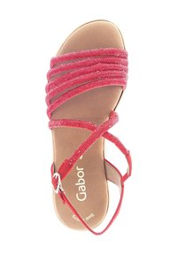 Red sandal with multiple textured straps, a cushioned beige footbed, and a metallic buckle accent. Minimalist design, open-toe style.