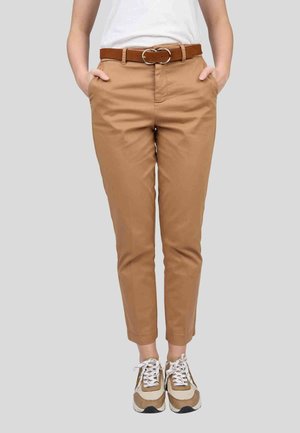 Pantalons en coton beige avec une coupe slim et une jambe effilée, dotés de poches latérales et d'une ceinture marron avec une boucle en argent. Associés à des baskets marron et blanches.