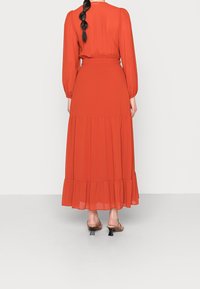 Długa, zwiewna, czerwona sukienka, wykonana z lekkiego materiału. Posiada długie rękawy, zaznaczoną talię i warstwowe falbany na dole.