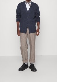 Námořnický cardigan s výstřihem do V, zapínáním na knoflíky a ribbovanými manžetami, v kombinaci s plaid béžovými kalhotami a černými botami s tlustou podrážkou.