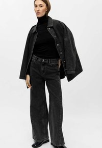 Black denim jacket with metallic buttons, worn over a black turtleneck and paired with high-waisted black wide-leg jeans. Glossy ankle boots.