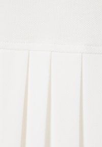 Gros plan d'un tissu blanc texturé avec des plis verticaux et une couture horizontale cousue près du haut.