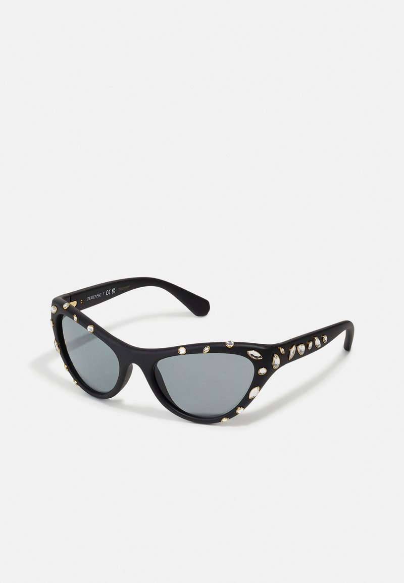 Óculos de sol estilo gato preto com lentes cinzas, decorados com strass dourados e transparentes ao longo da armação preta fosca.