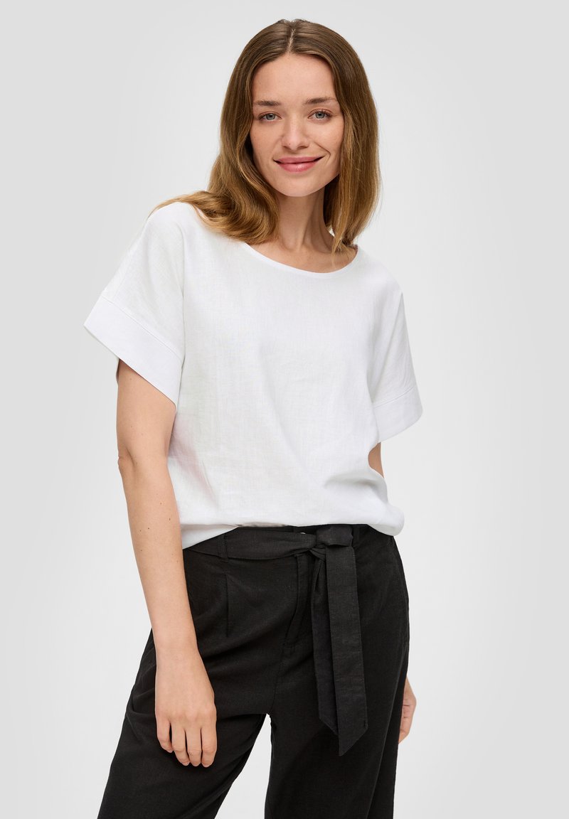 T-shirt en lin blanc avec un col rond large et des manches courtes, associé à un pantalon noir taille haute avec un détail de taille nouée.