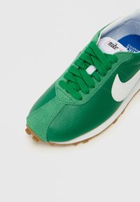 Sneakers verdes em pele com o logo swoosh branco, painéis texturizados verdes, atacadores planos e sola de borracha. Apresenta um tornozelo e uma língua almofadados.