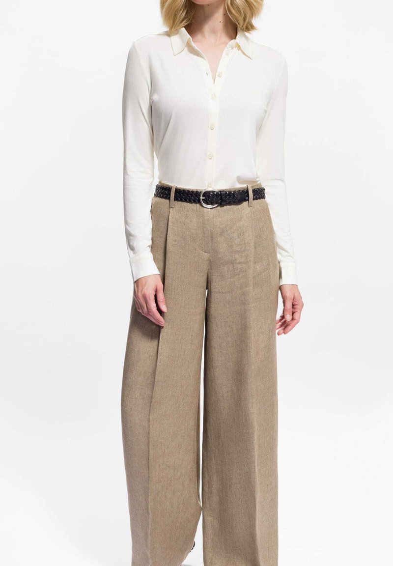 Witte blouse met lange mouwen en knopen, gecombineerd met beige linnen broek met hoge taille en brede pijpen, afgewerkt met een zwarte geweven riem met textuur.