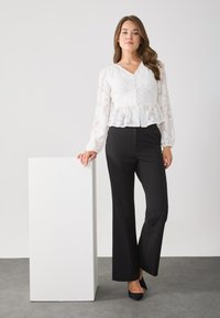 White textured blouse with long sleeves and peplum design, paired with black tailored trousers and black heels. Smooth, polished finish.