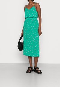 Tealblommig midiklänning med tunna axelremmar, elastisk midja, sidossprund, kombinera med kraftiga svarta sandaler och en svart handväska.