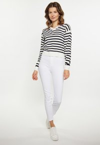 Pulover cu dungi alb-negru, de tip v-neck, cu mânecile lungi, asortat cu pantaloni albaștri ajustați și adidași albi. Aspect curat, casual.