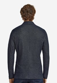 Mörknavy blazer med långa ärmar, skräddarsydd passform, slät textur och subtilt melerat mönster. Har en krage med snibbar och bakventiler.