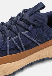 Marineblaue Sportschuhe aus strukturiertem Mesh und Wildlederakzenten, mit einer gepolsterten, hellbraunen Sohle und einer komplizierten Schnürung für einen sicheren Sitz.