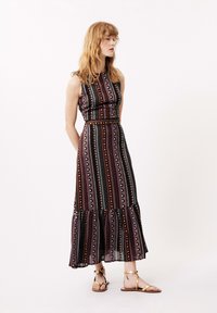 Maxi-Kleid mit einem taillierten Oberteil, das mehrfarbige vertikale Streifen, einen gerafften Saum und einen weichen, fließenden Stoff aufweist. Kombiniert mit beigen Sandalen.