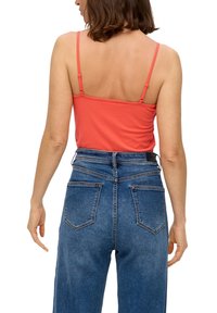 Top sans manches corail avec bretelles réglables et jeans taille haute bleus avec deux poches arrière et une finition en denim texturée.