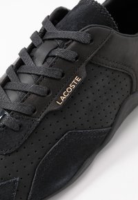 Baskets en cuir noir avec accents en daim, design perforé et fermeture à lacets avec logo "LACOSTE" doré. Semelles texturées.